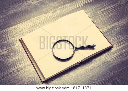 Book And Loupe On Wooden Table.