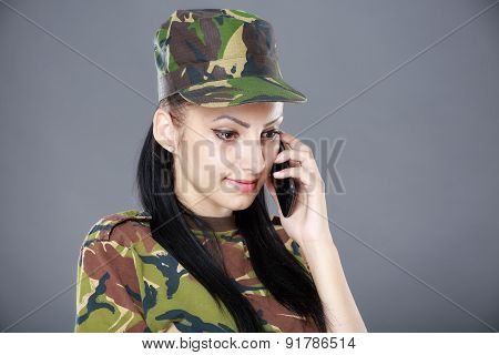 Image of attractive female soldier talking on cell phone against gray background