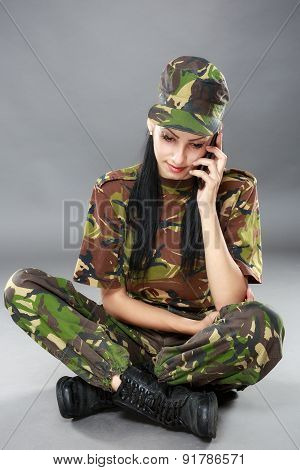 Image of attractive female soldier talking on cell phone against gray background