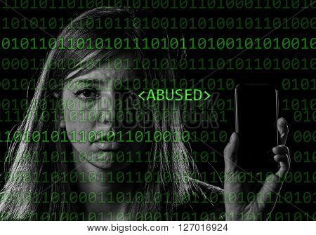 young scared and worried teenager girl holding mobile phone as internet stalked victim abused and cyberbullying or cyber bullying stress concept in binary code abused text black background