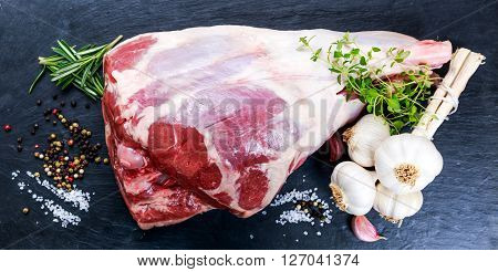 Raw lamb leg on blue stone background with herbs.