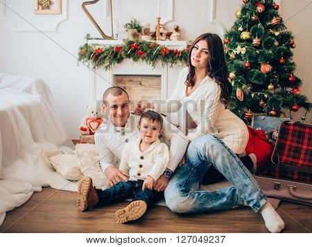 Beautiful family with little boy sitting in front of the Christmas tree