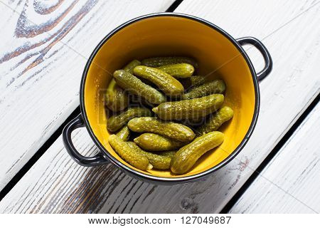 Pickles in a bowl. Bicolor bowl with pickled cucumbers. Vegetables on white kitchen table. Recipe of sour marinated pickles.