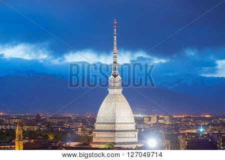 Cityscape of Torino (Turin Italy) at dusk with details of the Mole Antonelliana towering on the city and glowing in the night. Wind storm over the Alps in the background.
