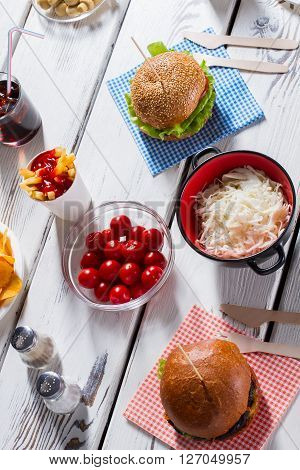 Burgers, pepperbox and tomatoes. Sauerkraut with burgers and cutlery. Lunch on white wooden table. Many shades of taste.