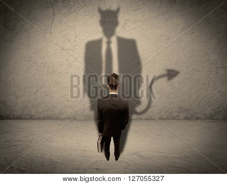 An experienced tricky businessman in suit looking at his devil desguise shadow reflected on the wall concept