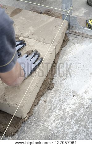 Construction Worker Lays The First Brick Of The Wall.