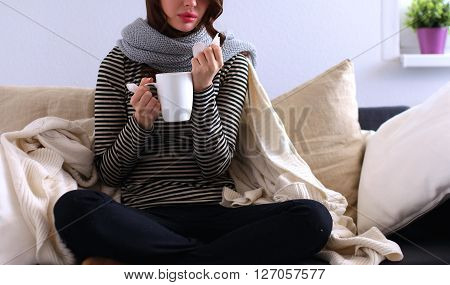 Portrait of a sick woman blowing her nose while sitting on the sofa.