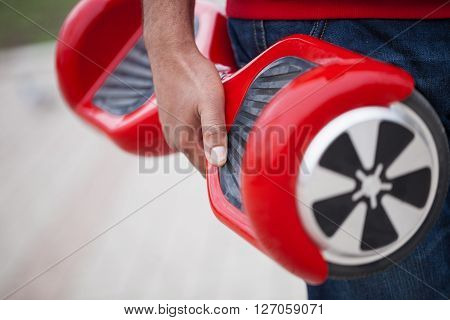 Man holding modern red electric mini segway or hover board scooter in hands. Trending new transportation technology that produces no air pollution to the atmosphere. African male model close up on device