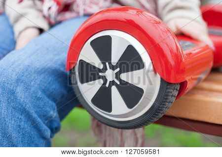 Woman in boho style clothes sitting on a benchwith modern electric mini segway or hover board scooter. Trending new transportation technology that is so much fun and easy to ride and produces no air pollution to the atmosphere. Focus on device