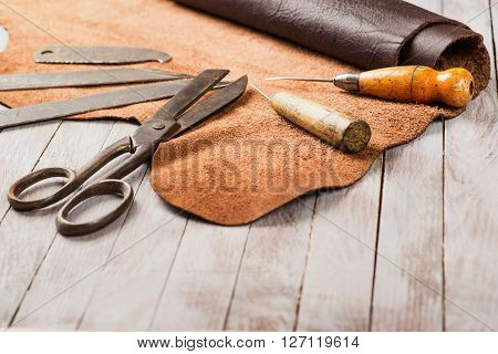 Leathersmith work desk . Pieces of hide and leather working tools on a work table.