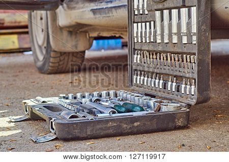 Open toolkit for car repair. Mechanic is going to begin repairing the car. He has put his toolbox near a car