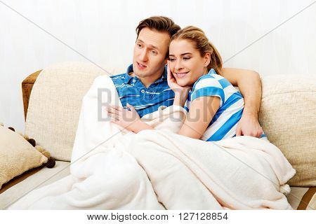 Smiling loving couple sitting on couch with blanket