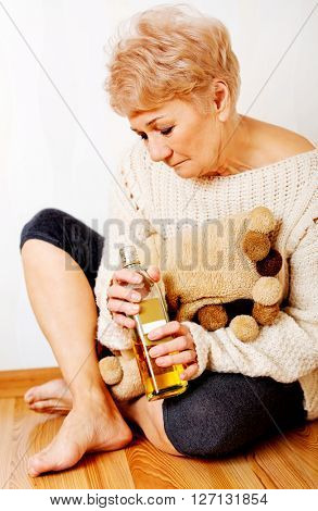 Elderly sad woman sitting in the corner and drinking whiskey