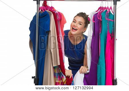 Beautiful happy young woman lookinh through hanger with many dresses. Isolated over white background. Copy space.
