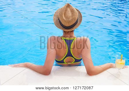 Pretty brunette woman in a hat enjoying lemonade in a swimming pool