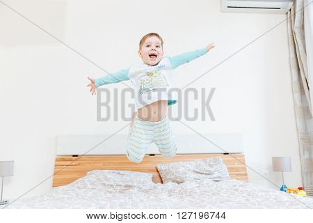 Happy little boy jumping on bed in bedroom