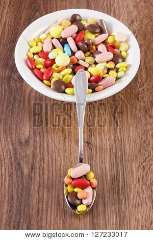 Colorful medical pills on teaspoon and tablets capsules or supplements for therapy on plate concept of treatment and health care