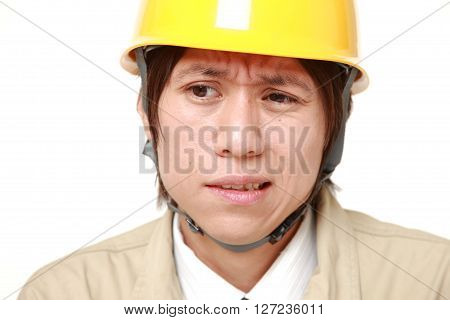 perplexed young Japanese construction worker on white background