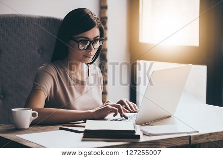 Concentrated at work. Young beautiful woman using her laptop while sitting in chair at her working place