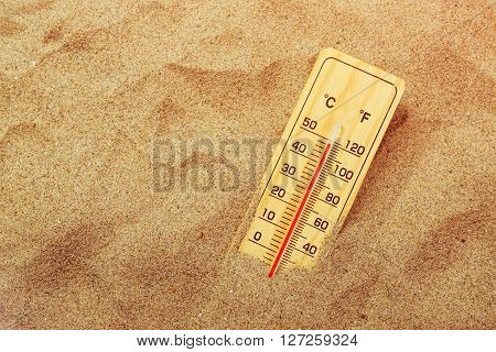 Thermometer with celsius and farenheit scale on warm beach sand showing record extreme high temperatures