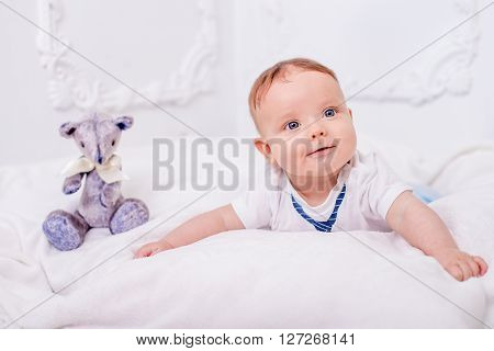 Baby lying on tummy and looking at the camera on a white background. Bear sits right baby