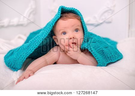 Cute baby under a blanket on the white wall