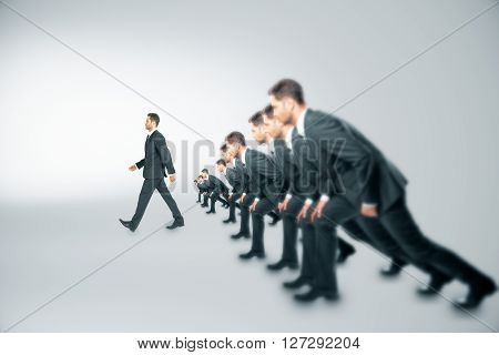 Competition concept with many businessmen about to run and one walking ahead of them on grey background