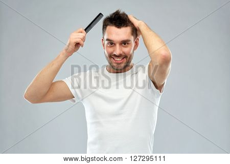 beauty, grooming and people concept - smiling young man brushing hair with comb over gray background