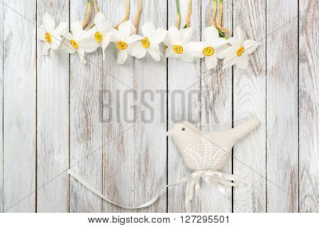 Narcissus flower, decorative bird on a light wooden background. Selective focus. Space for the text.