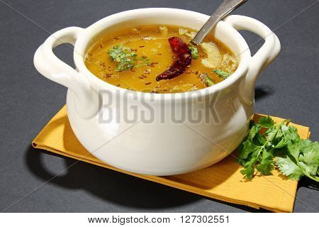 Arhar Daal soup with tempering of red chili cumin seeds and garlic with cutter on a moody background with copy space.