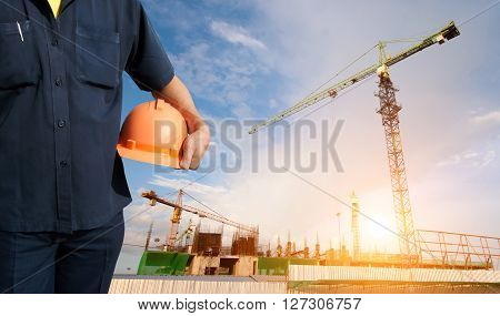 engineer holding orange helmet on background of new office buildings and construction cranes in blue sky - Sunlight filter effect