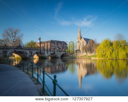 View along the river Severn to the English Bridge, Shrewsbury and a church and prominent willow tree, England, UK.