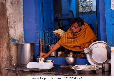 VARANASI, INDIA - JANUARY 2, 2013: Indian milkman prepares the popular drink Lassi by an ancient recipe sitting on a doorstep on January 2, 2013. Varanasi urban agglomeration had a population of 1435113