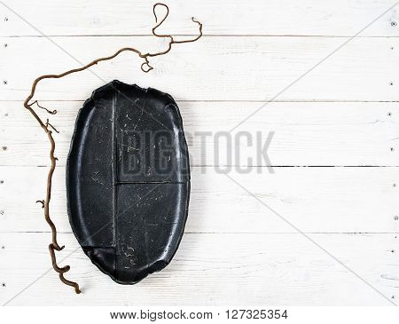 Top view empty black oval plate on rustic wooden table. Ceramic creative black plate on white wooden background with free space. Flat lay of handmade black dish on white wooden table.