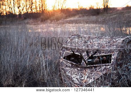 Hunting tent with hunters lurking waiting for prey in the field next to the river while picturesque sunrises