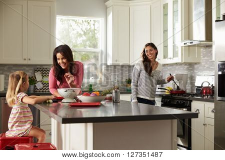 Girl with her female parents, preparing meal in the kitchen