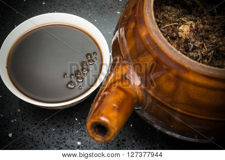 bowl of Chinese herbal tea and an enamel pot with herbs nearby
