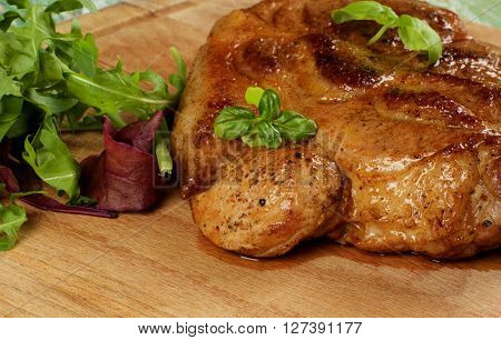 Delicious Juicy Roasted Pork Neck with Fresh Arugula Mangold and Basil closeup on Wooden Cutting Board