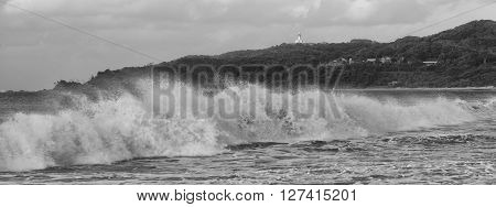 Black and white image of Byron Bay beach and waves in New South Wales, Australia with Cape Byron lighthouse in the background.