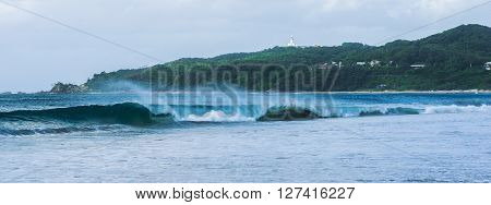 Byron Bay beach and waves in New South Wales, Australia with Cape Byron lighthouse in the background.