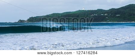 Byron Bay beach and waves in New South Wales, Australia with Cape Byron lighthouse in the background.