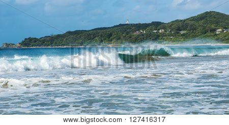Byron Bay beach and waves in New South Wales, Australia with Cape Byron lighthouse in the background.