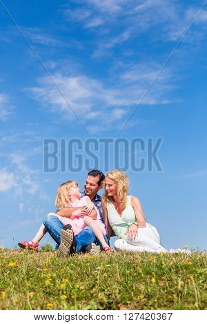 Parents and daughter sitting on grass, total view, centred, centered