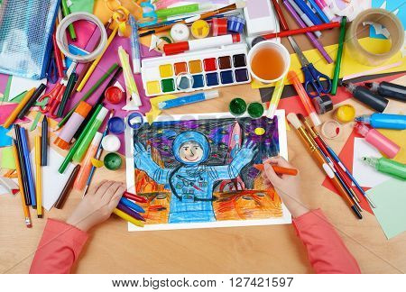 child drawing astronaut exploring the red planet, space concept, top view hands with pencil painting picture on paper, artwork workplace