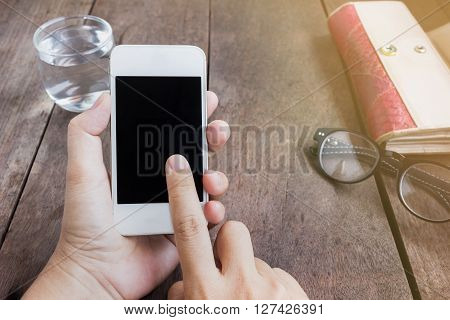 Lady hand serfing internet on mobile phone with background of things on wood table and copy space