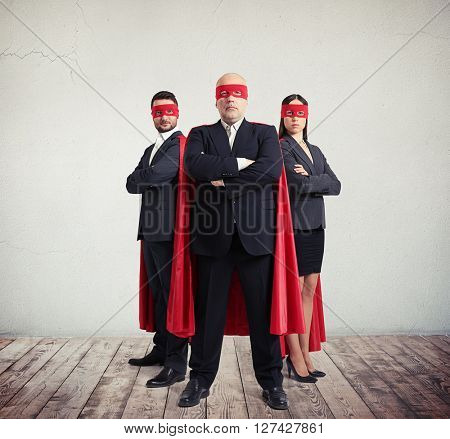 Two businessmen and businesswoman in superhero costume staying side by side with arms folded