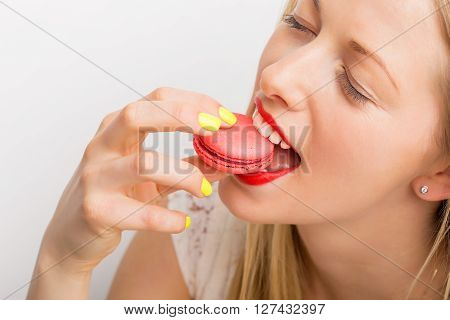 Happy and beautiful woman eating pink macaroon cookie