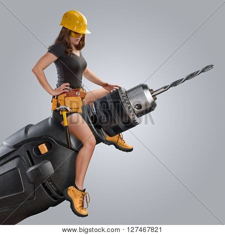 worker girl sitting on a drill on grey background