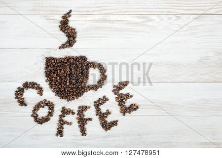Coffee beans making a word coffee and shape of cup of fragrant hot coffee on wooden background